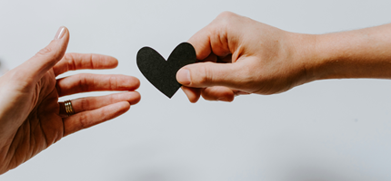 Two hands reaching toward each other, with one holding a paper heart.