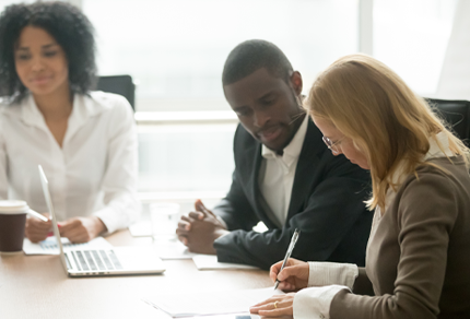 Three professionals meeting at a conference table while reviewing documents and taking notes.
