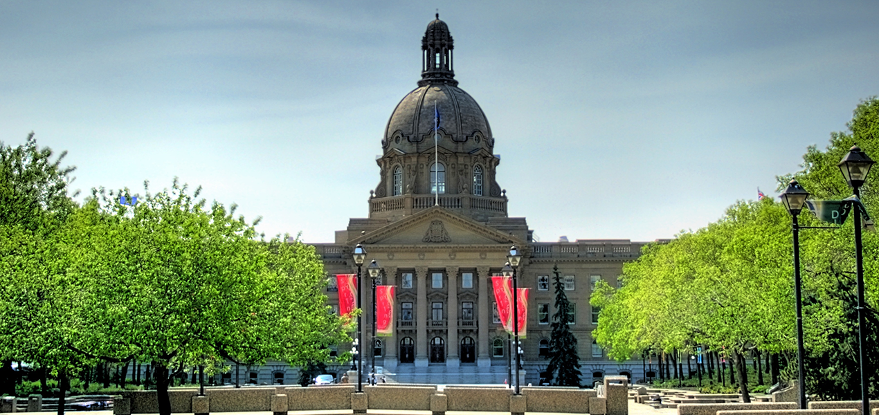 A front view of the Legislature building in Edmonton, with green leafy trees on either side.