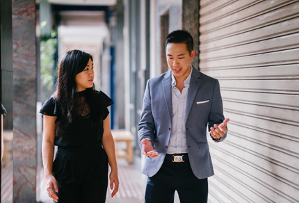 An Asian female and Asian male dressed in business attire walking outside and talking to each other.