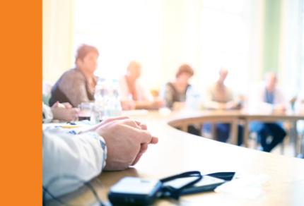  Locally Uploaded Image  This image was uploaded directly to AltText AI for processing. 	  People are seated around a curved conference table in a brightly lit room, with focus on hands in the foreground and blurred figures in the background. 