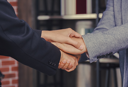 Two people in business attire clasping hands in a supportive manner.