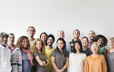 A group of people sit around a large conference table in a bright room, with documents and microphones on the table.