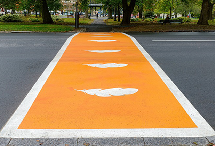A vibrant orange crosswalk features white feather designs, representing truth and reconciliation with Indigenous peoples.