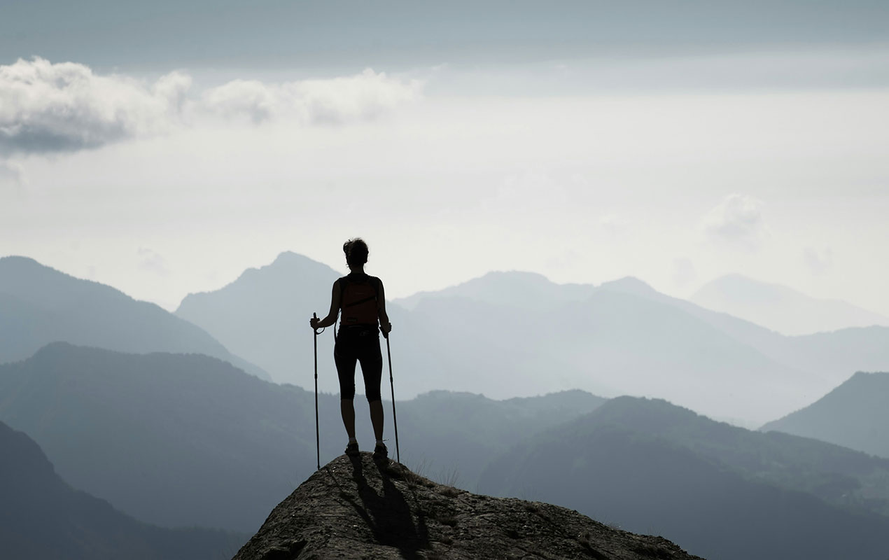 A climber standing at the top of a mountain looking across the sky at the distant horizon.