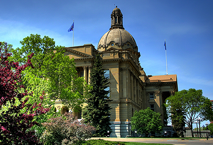 A front view of the Legislature building in Edmonton, with green leafy trees on either side.